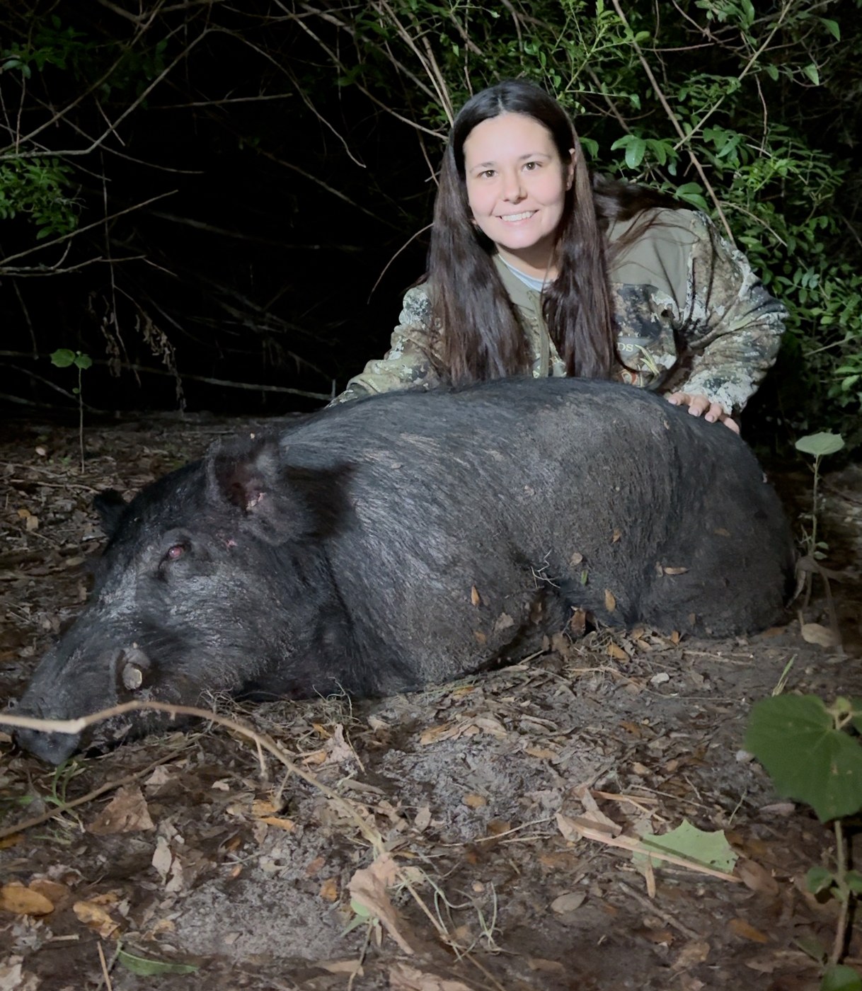 McKenzie crouched behind a wild hog she harvested at night, one hand resting on it